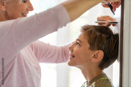 Mother measuring the height of her son against wall at home 