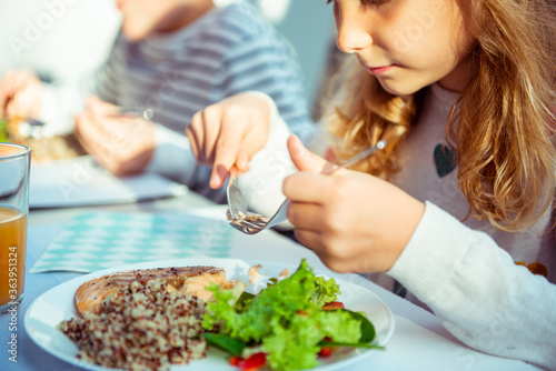 Close up photo of hands of child girl eating healthy dinner with salad, quinoa and fish