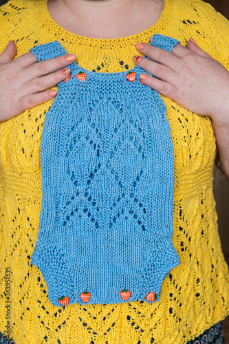 Women's hands gently pressed to the chest knitted blue jumpsuit for a newborn.