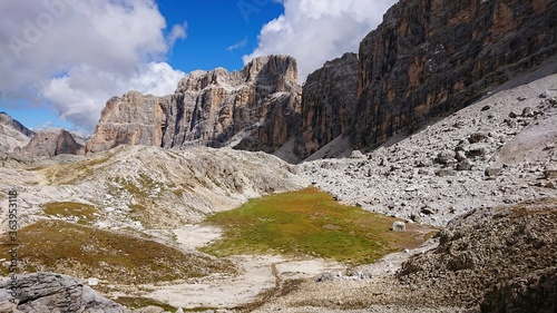 Summer landscape of Italy Dolomites. Gray mountains with natural shadows, and islets of fresh green vegetation in the valley