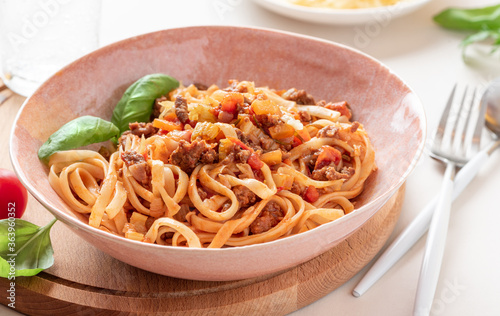Pasta Bolognese. Tagliatelle with homemade bolognese sauce of minced meat, tomatoes, celery, carrots and spices in a bowl on a white served table close-up. Italian Cuisine.