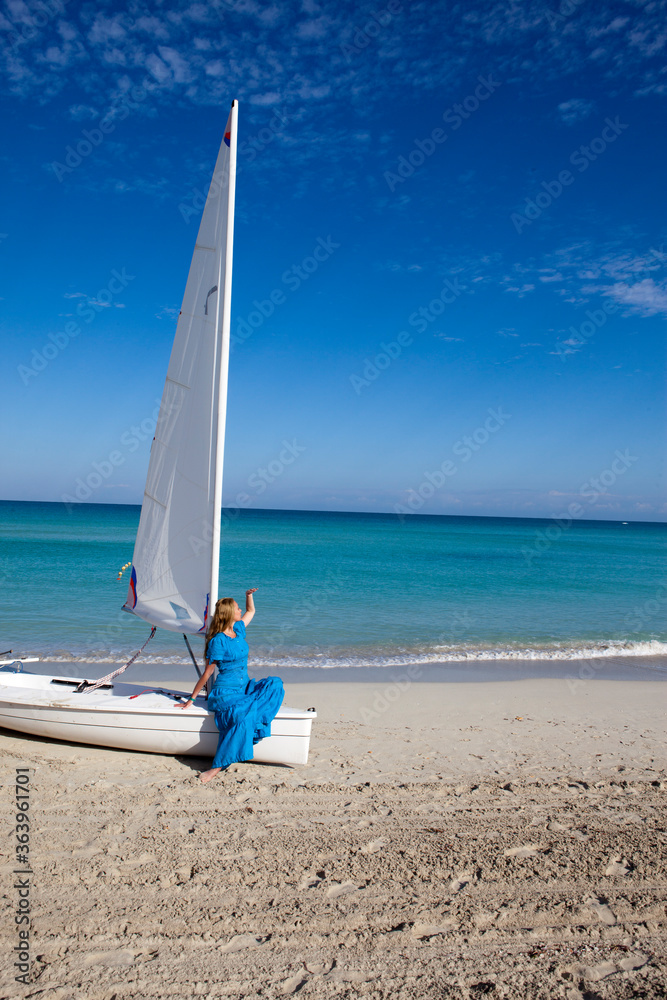 Fototapeta premium Cuba. Beautiful woman on the blue sea near the boat with a sail