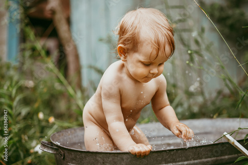 Vászonkép a little boy bathes in a basin in the summer in a green garden.