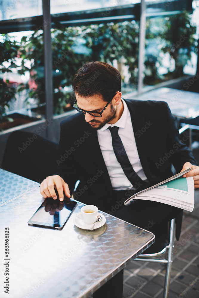 Portrait of a young successful businessman sitting in an coffee shop and using a digital tablet, business man having breakfast sitting on beautiful terrace with plants