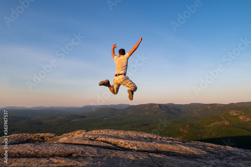 Back view of a man jumping at the summit of "La Chouenne" mountain in Charlevoix, Quebec