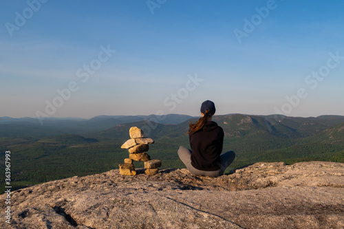 Young woman sitting next to an Inukshuk at the summit of "La Chouenne" mountain in Charlevoix, Quebec