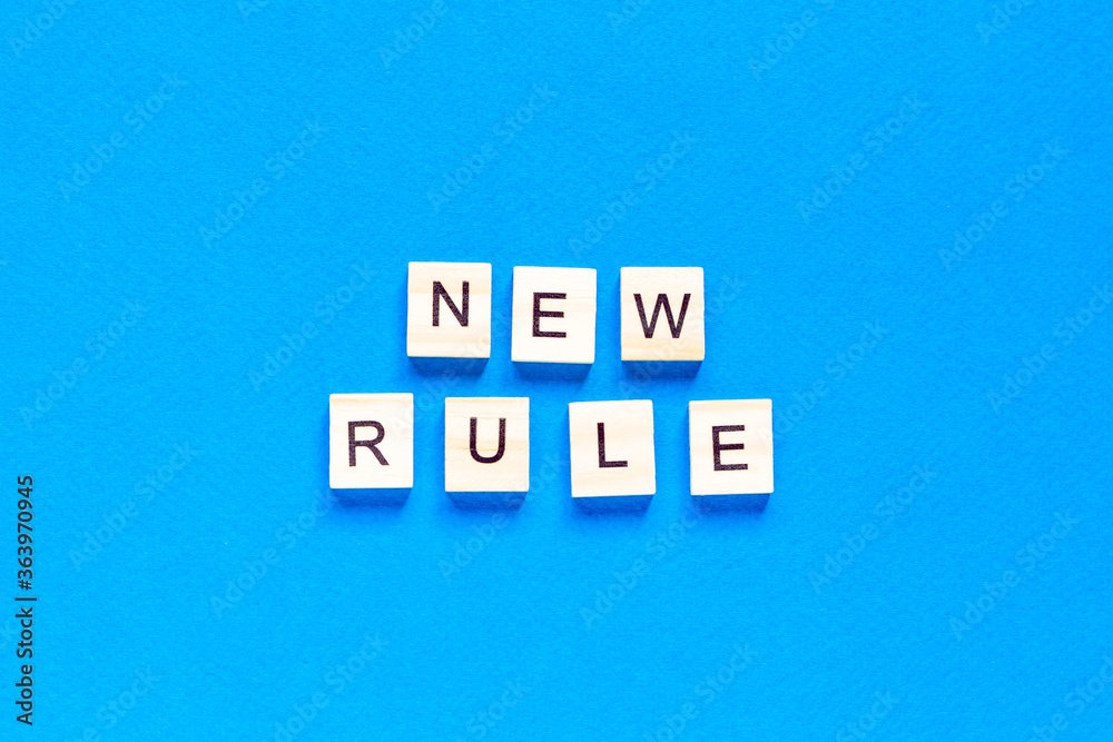 The NEW RULE is written in wooden letters on a blue background. New concept. Business, law, rules, update. top view. flat layout. The NEW RULE is written in wooden letters on a blue background. New concept. Business, law, rules, update. top view. flat layout.