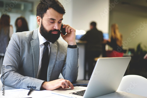 Confident bearded businessman calling to colleague checking financial reports in online database using laptop computer, manager of IT corporation calling to candidate making job offer for vacancy