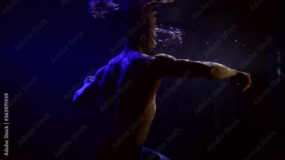 Close-up portrait of a dark-skinned, muscular man with a naked torso. They are on a dark blue background with bubbles that swims and dances beautifully. It is reflected from the surface of the water. Close-up portrait of a dark-skinned, muscular man with a naked torso. They are on a dark blue background with bubbles that swims and dances beautifully. It is reflected from the surface of the water.