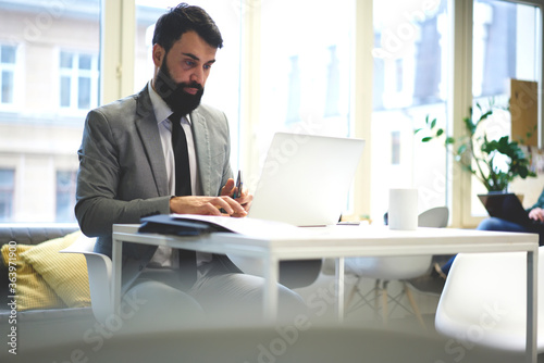 Professional concentrated male entrepreneur checking email box typing feedback on laptop computer, handsome businessman transferring money in online banking service using laptop computer and wifi
