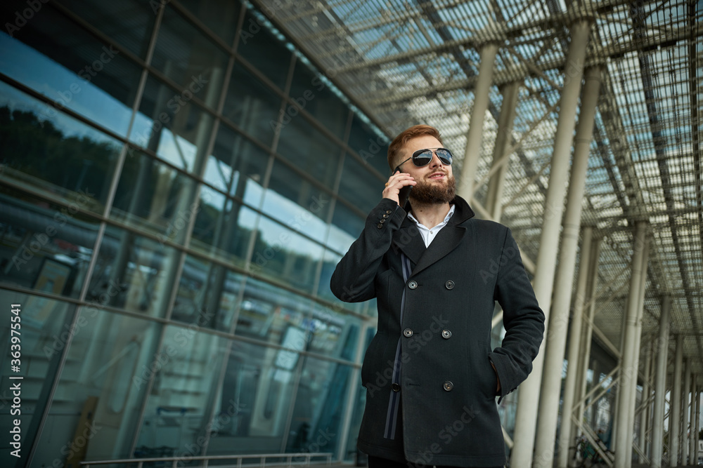 Urban business man in sunglasses talking smart phone traveling walking outside airport. Casual young businessman wearing suit jacket. Handsome male model in 20s, Manager, City Hall, cell. Urban business man in sunglasses talking smart phone traveling walking outside airport. Casual young businessman wearing suit jacket. Handsome male model in 20s, Manager, City Hall, cell.