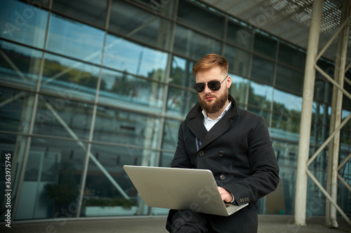 Manager holding laptop, Out of office work, young businessman in sunglasses using computer for his job at outside. Handsome bearded hipster, Communication and technology, in the open air, Surfing