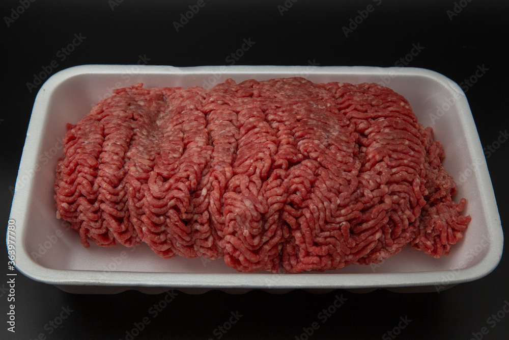 Raw minced (ground) meat in a white styrofoam box isolated on black background with copy space for text Raw minced (ground) meat in a white styrofoam box isolated on black background with copy space for text