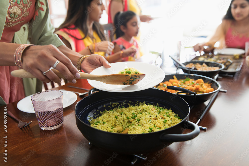 Indian women in saris serving and eating food at table Indian women in saris serving and eating food at table