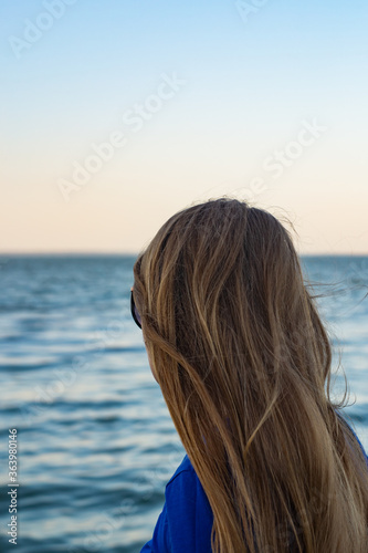 young blonde girl looking sea and blue skies back view
