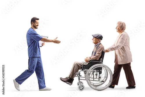 Full length profile shot of a male health worker walking and welcoming elderly man in a wheelchair