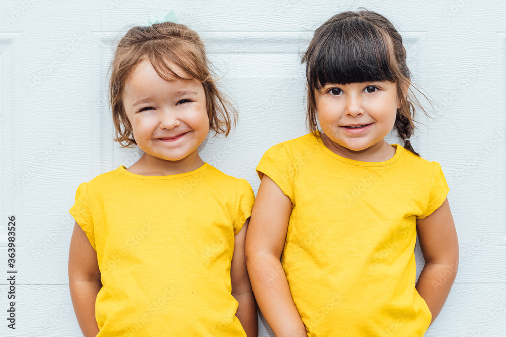 Adorable twin girls wearing a yellow shirt leaning against white background Adorable twin girls wearing a yellow shirt leaning against white background