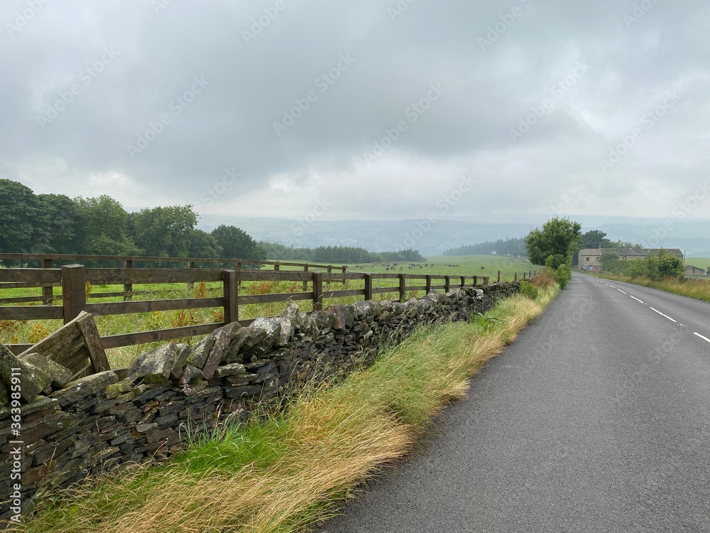 A country road, with dry stone walls, fields, and heavy rain clouds near, Slaithwaite, Huddersfield, UK