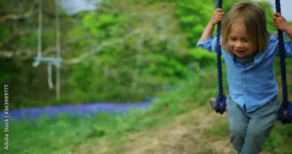 Mother helping her preschooler use a rope swing in a meadow Mother helping her preschooler use a rope swing in a meadow