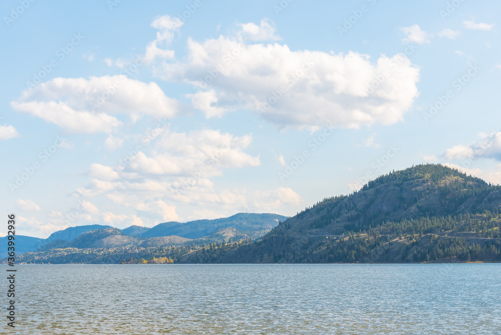 View of calm lake, forested mountains, and blue sky with clouds.