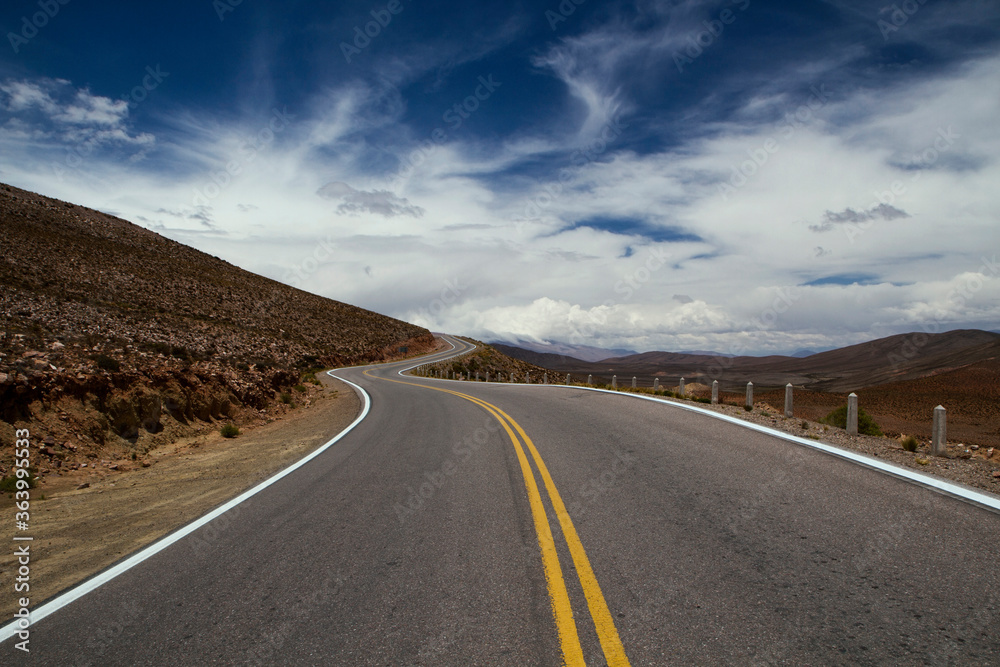 Getaway. Artistic view of the asphalt road across the desert and hills under a dramatic sky.  