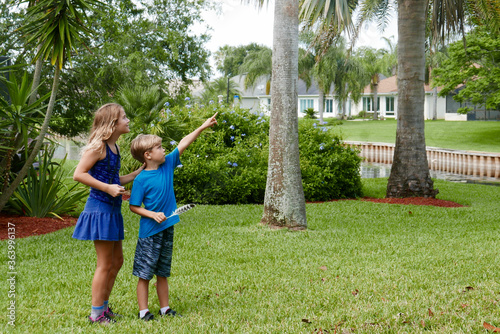 Children exploring nature in their neighborhood, collecting scavenger hunt items and pointing at a bird nest