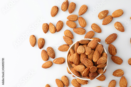 Almonds nut seed in white bowl flat lay top view heap on white background with copy space on the left. Snack whole healthy food is useful to help neutralize free radicals and provide energy.