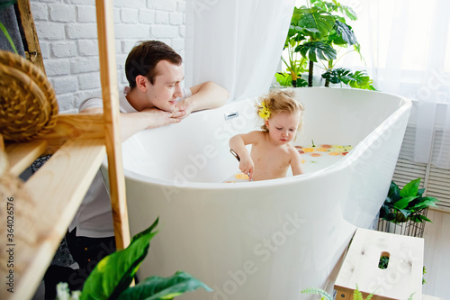 фотографія A cute little girl is sitting in a bath with milk and orange and yellow fruits and flowers