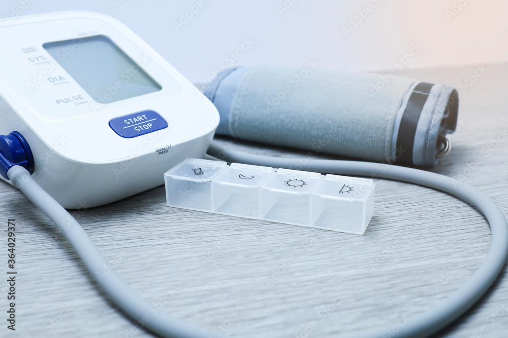 Pills container and blood pressure monitor on wooden table Pills container and blood pressure monitor on wooden table