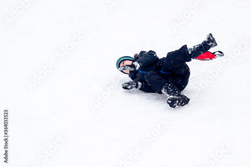 Baby boy rides from a snow slide on a red cardboard. Fun games in the snow. Snowy winter in Russia. Happy child having fun.