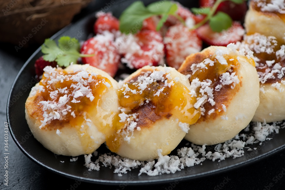 Closeup of fried cheesecakes or syrniki with jam, coconut flakes and strawberries, selective focus, studio shot