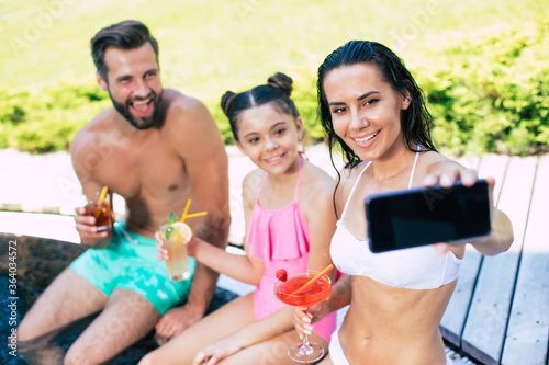 Smiling beautiful young happy family making selfie on smart phone while they resting in the hotel pool and have fun.