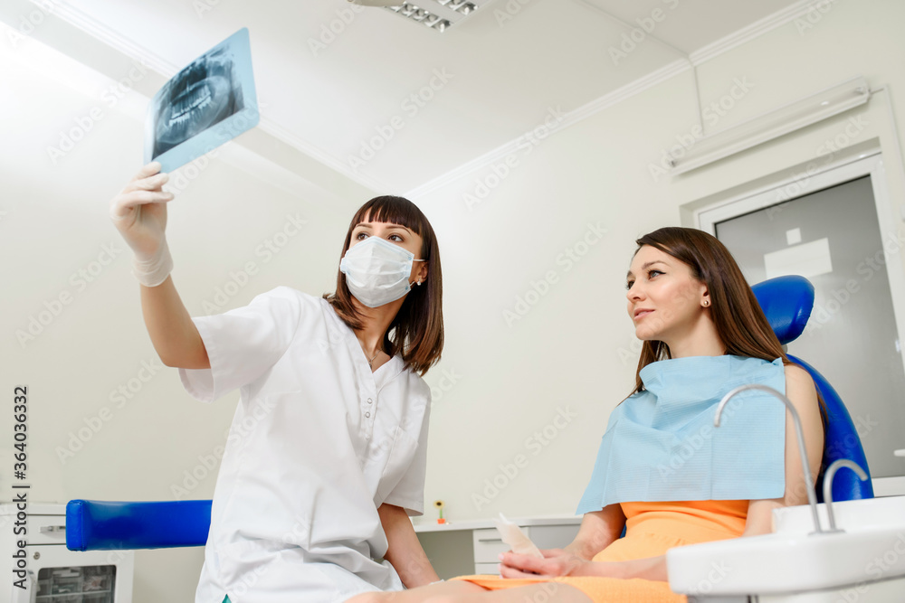 Obraz premium Young woman dentist explaining to her patient on a dental x-ray panoramic radiography all the dental treatment that needs to do in dentistry