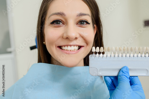 The dentist is checking the color with the tooth color chart of the patient