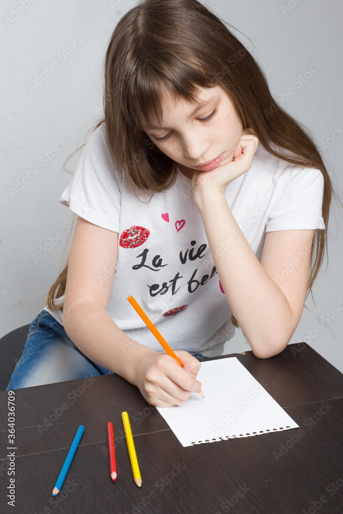 young girl child sitting at the table, drawing in notebook