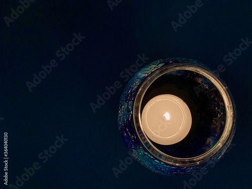 A Candle fire light lighting bright in the glasses cup on black background indoor