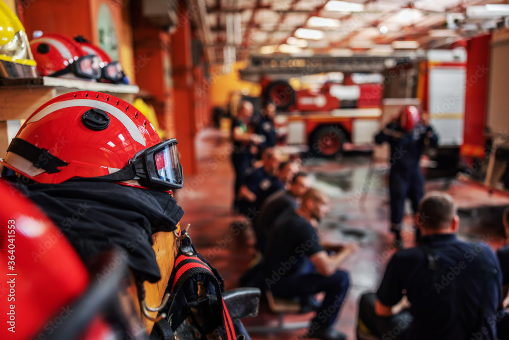 Obraz premium Closeup of firefighter sitting and listening boss who is talking about tactic how they gonna extinguish the fire. Fire brigade interior. Closeup of protective suit and helmet.