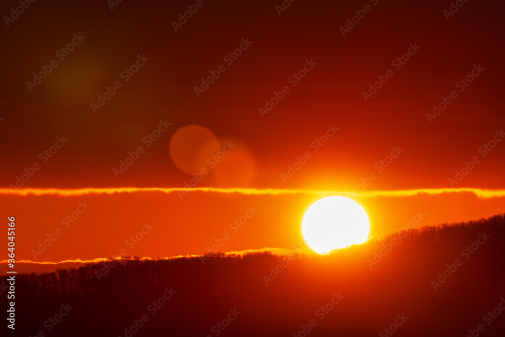Beautiful sunrise in mountains, red orange sun disk rises from tops of mountain range. Natural lens flare in sky, sunbeam light leaks.