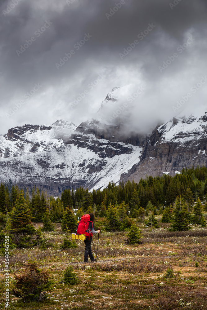 Female Backpacker Hiking in Canadian Rockies during a cloudy day. Taken near Banff, boarder of British Columbia and Alberta, Canada. Concept: Explore, Adventure, Trekking, Backpacking