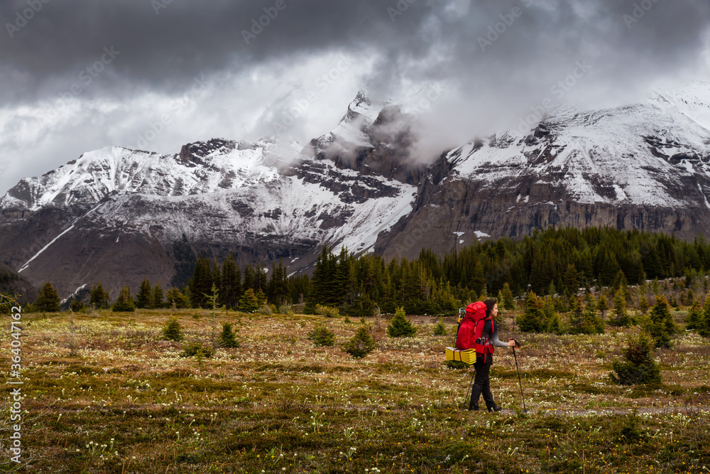 Female Backpacker Hiking in Canadian Rockies during a cloudy day. Taken near Banff, boarder of British Columbia and Alberta, Canada. Concept: Explore, Adventure, Trekking, Backpacking