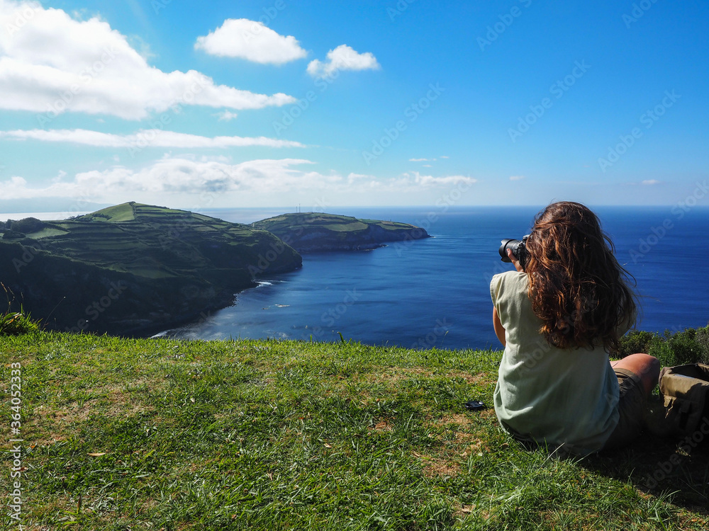 Chica joven de espaldas haciendo fotografías de la costa de la isla de San Miguel en las Azores