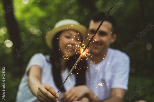 A young international couple in love while relaxing outdoors in a Park in summer with a bright Sparkler. Bluer.