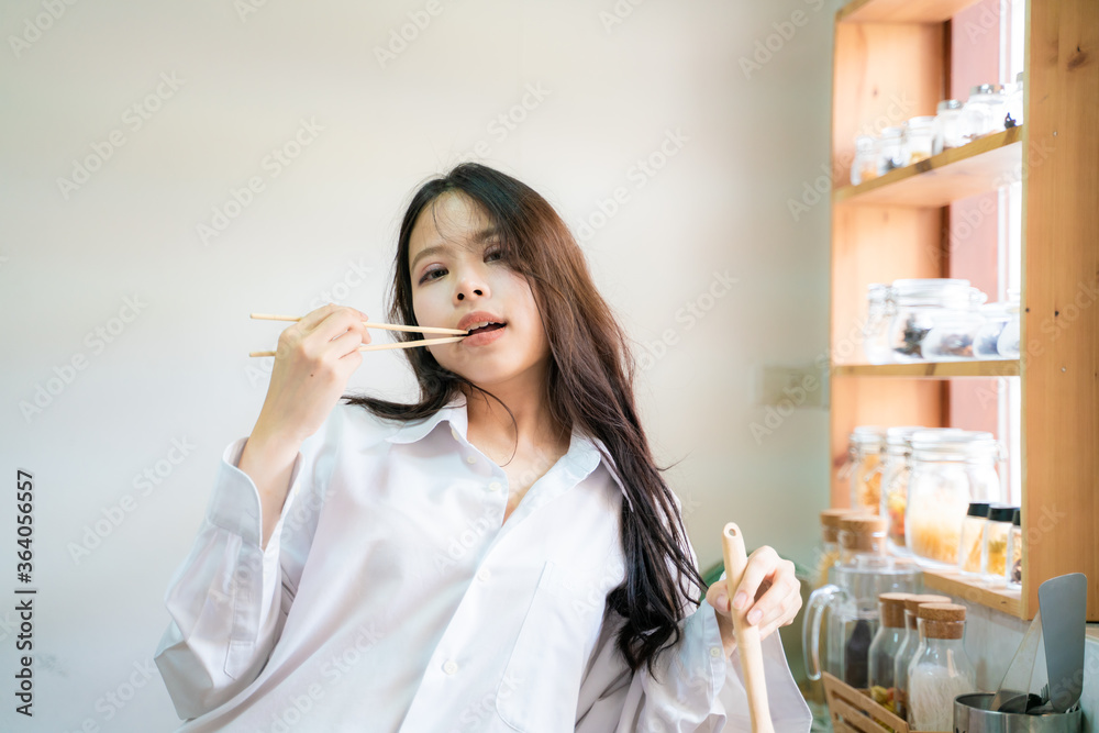Beautiful asian casual girl is tasting food and smiling while cooking in kitchen Beautiful asian casual girl is tasting food and smiling while cooking in kitchen