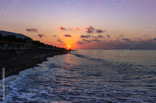 Santorini, black pebble beach of Perivolos, Perisa at sunrise. Sea waves, beach chairs and umbrellas, beautiful sky with clouds. photo