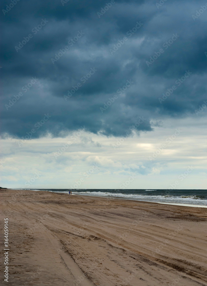 Couple walking along the ocean shore against a dramatic sky.