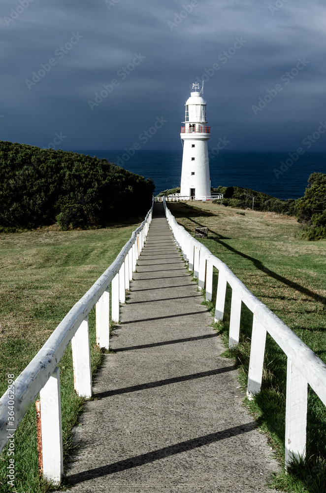 Path leading up to a lighthouse with dark stormy sky in the background