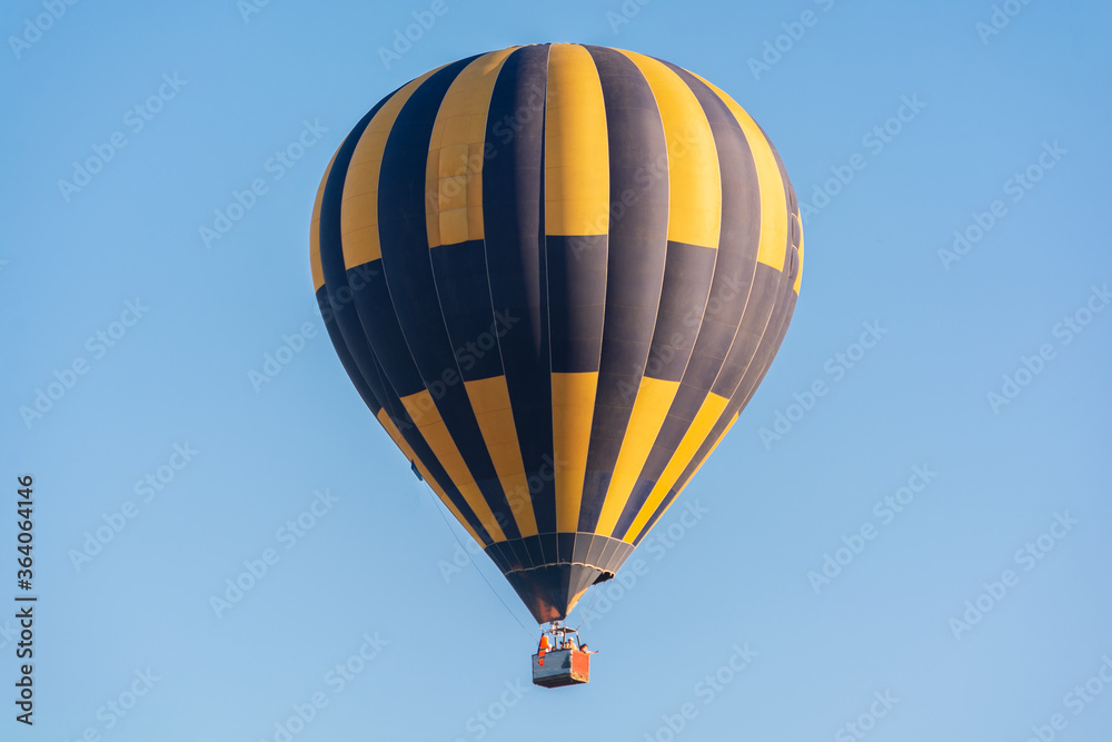 Naklejka premium Balloon flying high in the sky. Balloon basket with people. Aeronautic sport. Burning gas. Bright multi-colored balloon. Romantic trip. Free space for text.