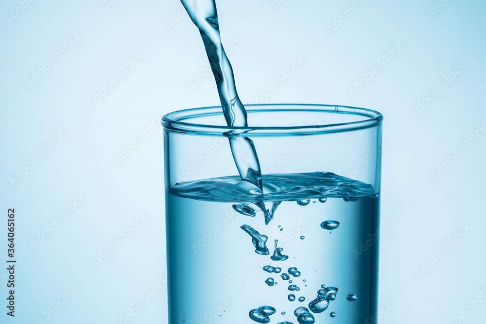 close up of pouring water into glass on blue background. close up of pouring water into glass on blue background.