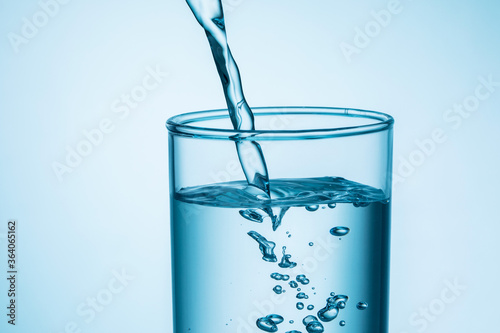 close up of pouring water into glass on blue background.