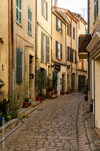 Narrow street in a small Provencal village. The granite paving has shiny reflections. Some shop windows and their sign.